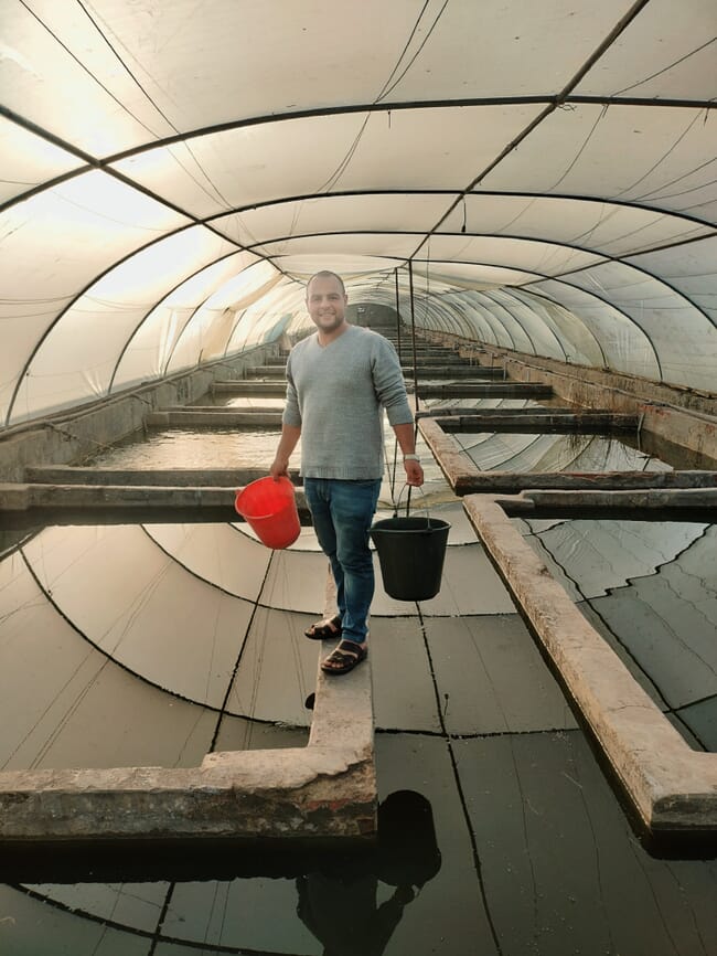 A man standing in a fish farm within a polytunnel.