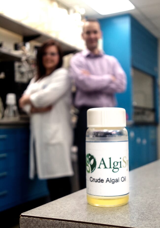 A bottle of oil, with two people in the background.