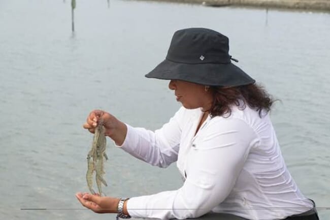 A woman holding some shrimp above a pond.