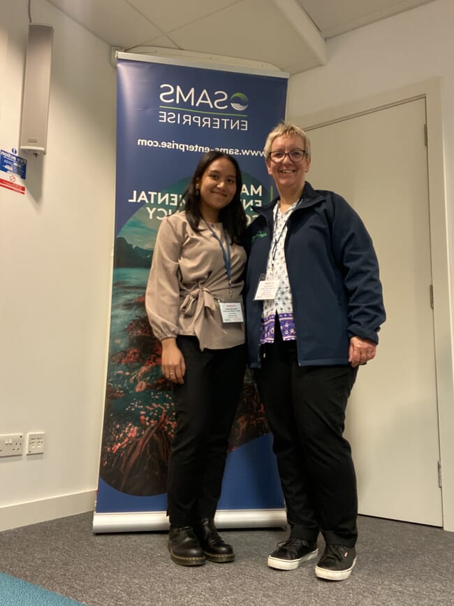 Two people in front of an event poster.
