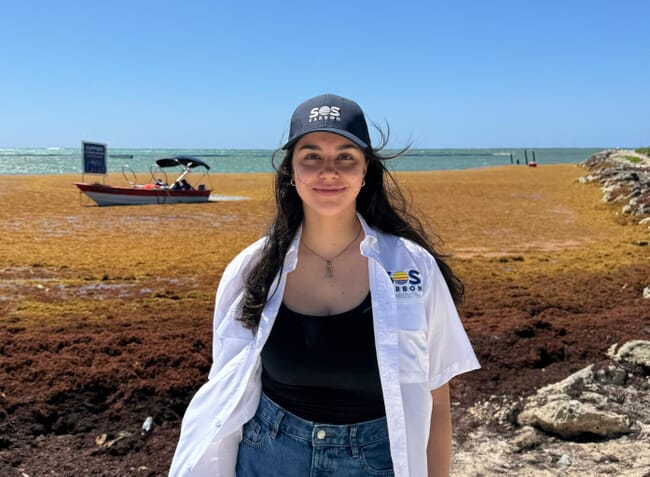 A woman standing on a seaweed covered beach.