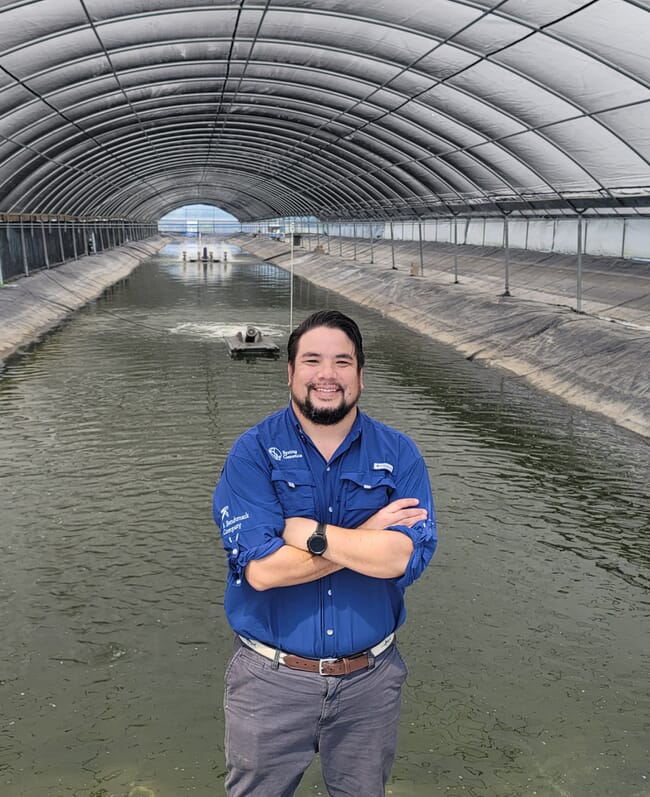 A man standing in front of several large covered fish ponds.