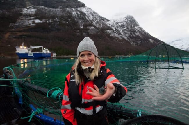 a lady holding a lumpfish while standing on a floating salmon pen