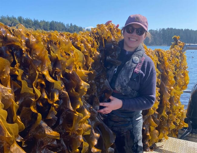 A woman standing beside a large crop of seaweed.