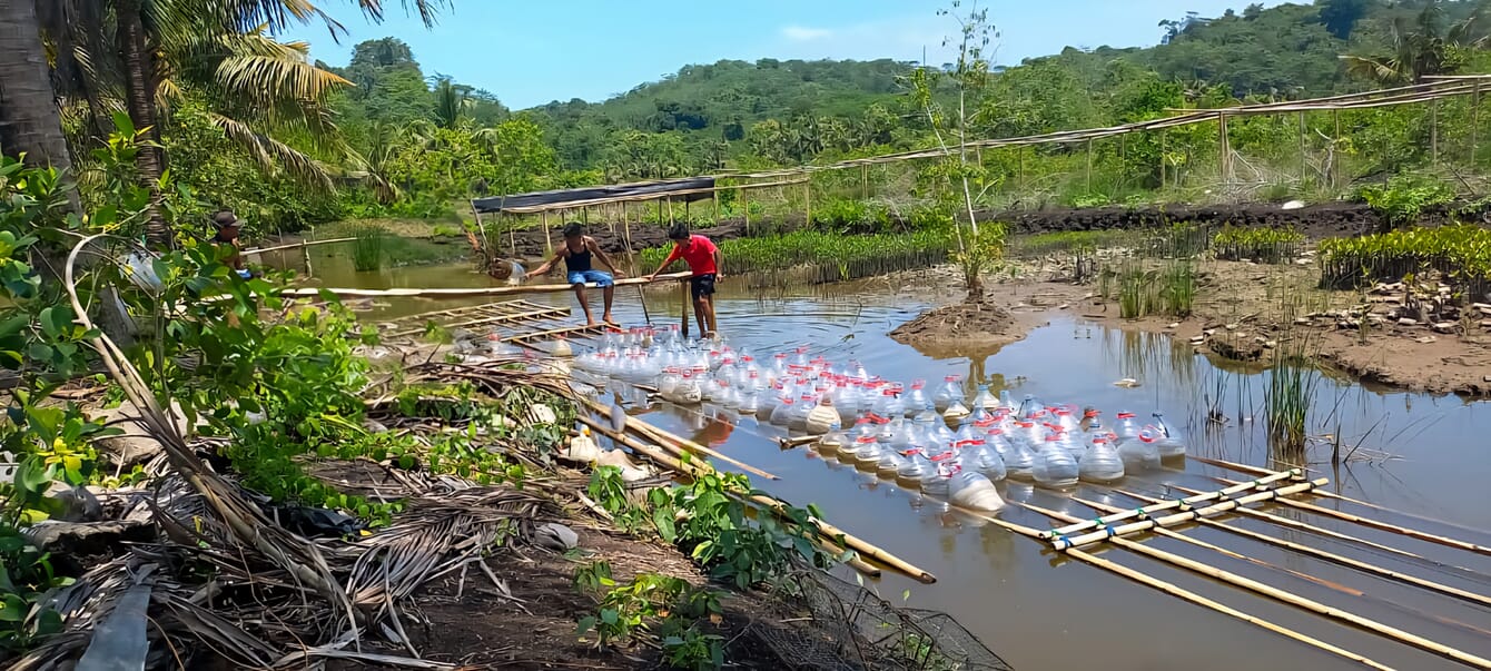 Two people beside a pond filled with bottles.