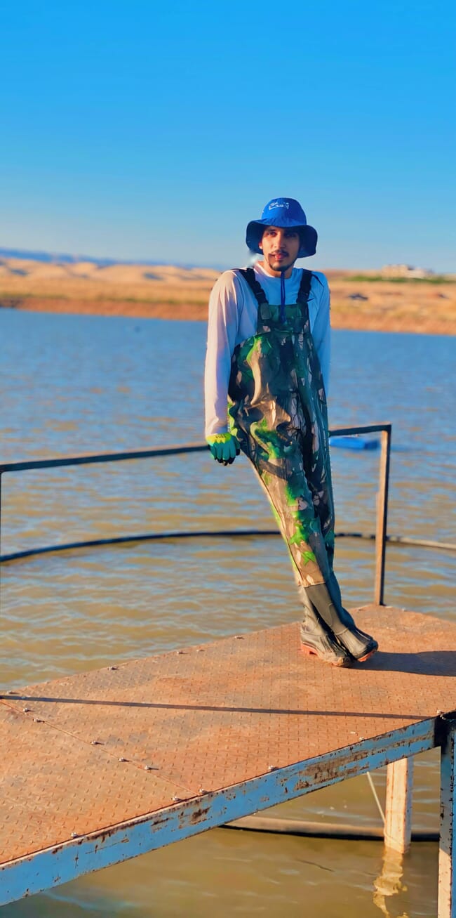 A man in a hat standing beside a pond.