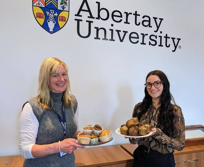 Two women holding platters of muffins.