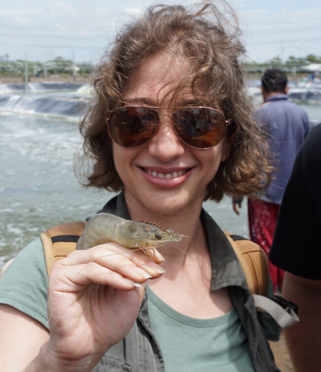 A woman holding up a shrimp on her hand.