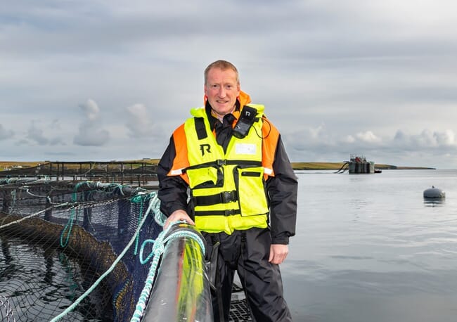 A man standing on the edge of a fish pen in the sea.