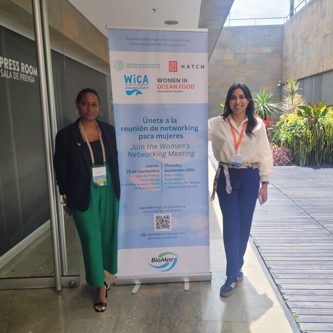 Two women standing beside a sign.